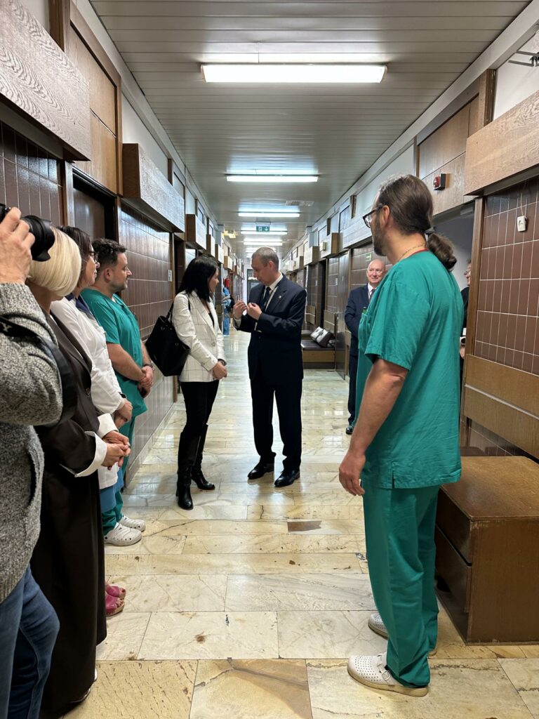 Zdjęcie przedstawia grupę osób zgromadzonych w nowoczesnej sali szpitalnej podczas prezentacji sprzętu medycznego