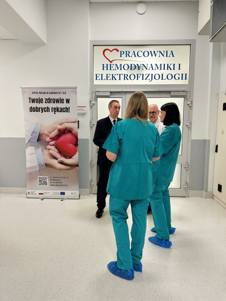 Zdjęcie przedstawia grupę osób zgromadzonych w nowoczesnej sali szpitalnej podczas prezentacji sprzętu medycznego