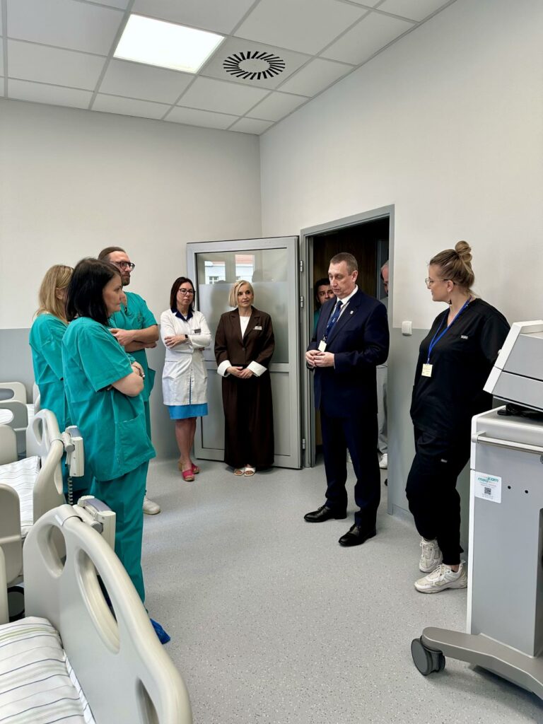 Zdjęcie przedstawia grupę osób zgromadzonych w nowoczesnej sali szpitalnej podczas prezentacji sprzętu medycznego